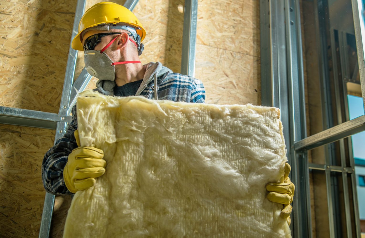 Caucasian Construction Worker Wearing Safety Mask Moving Pieces of Mineral Wool Insulation.